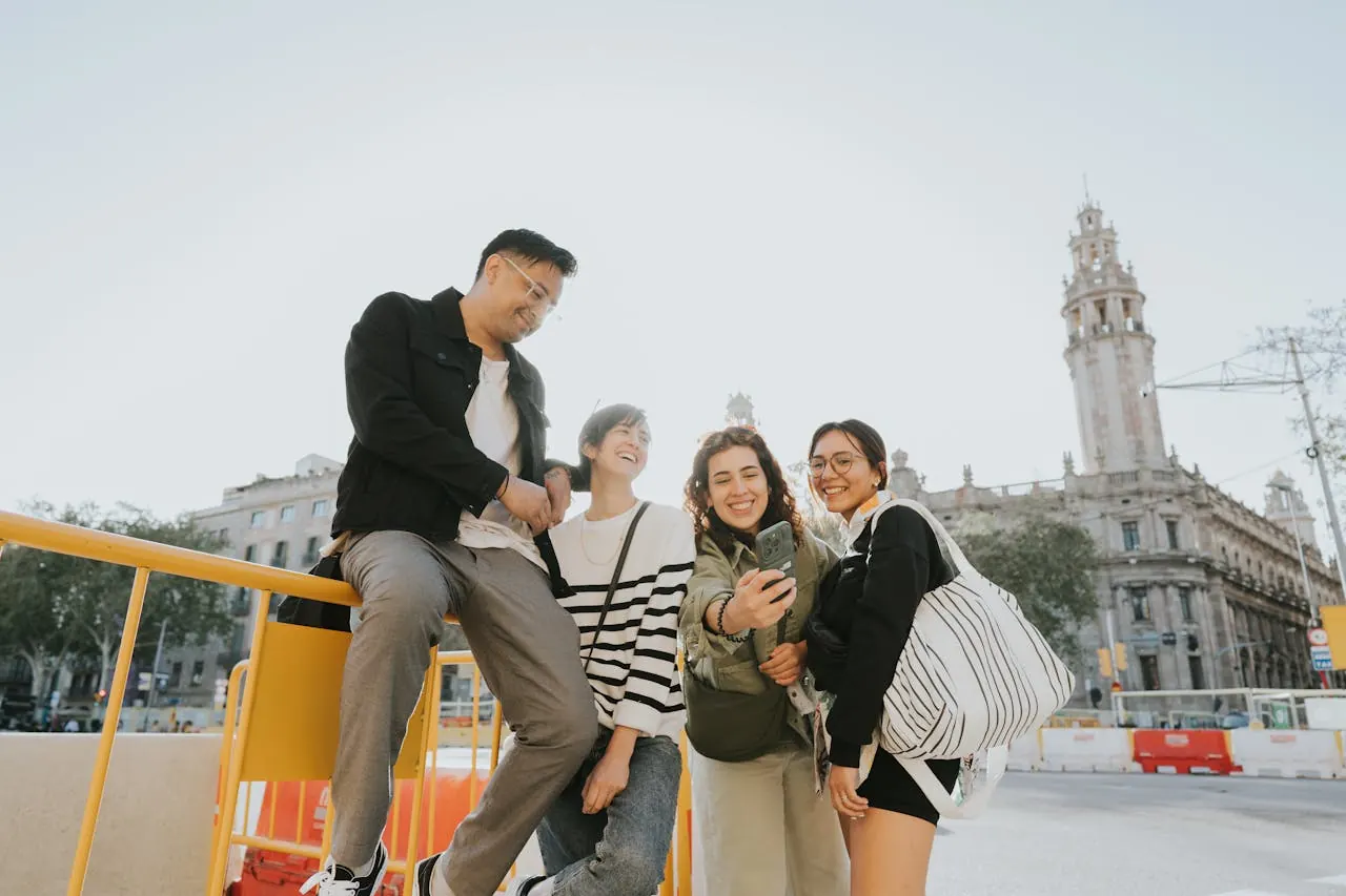 four travelers gathered around a phone on a sunny Barcelona street