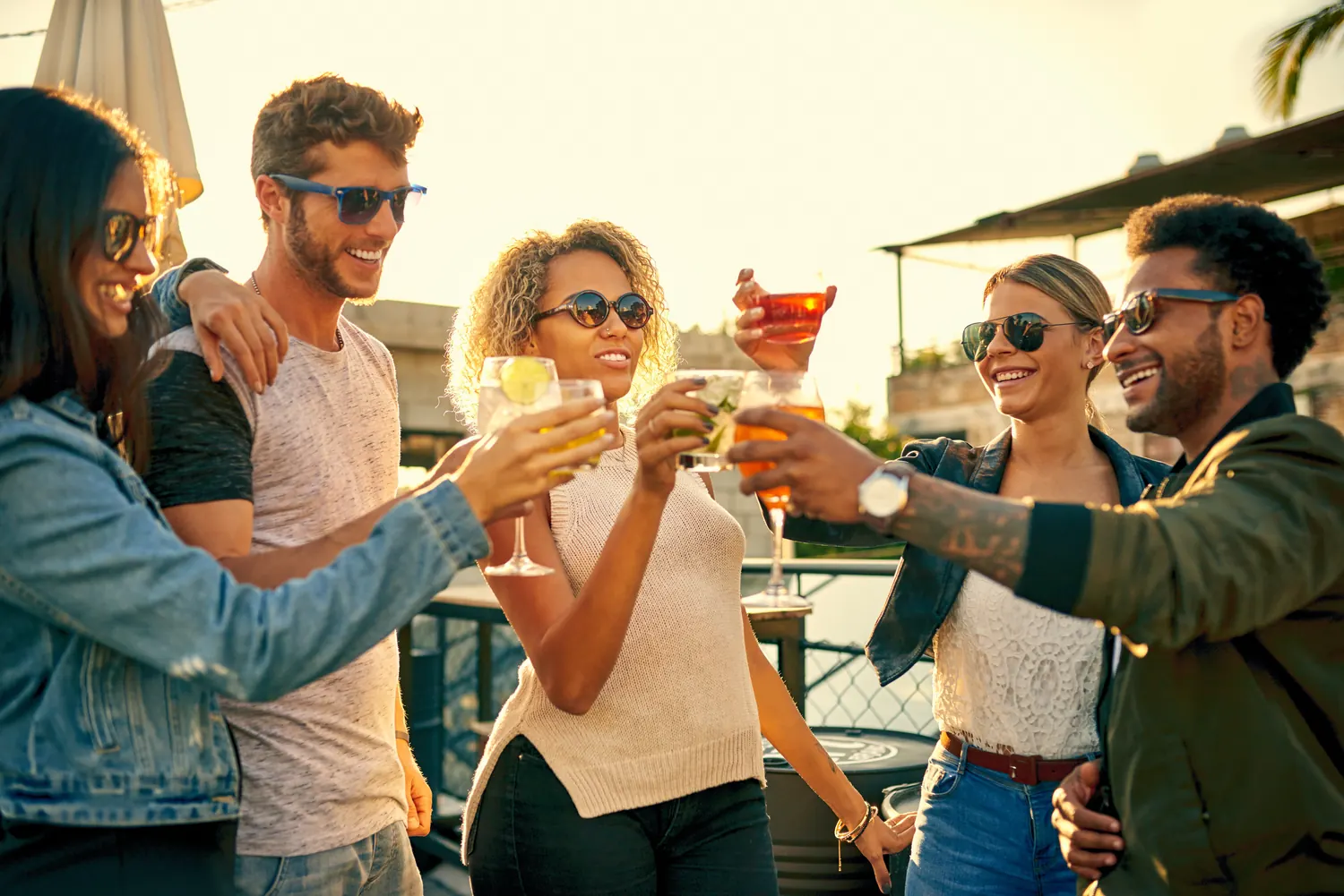 A group of travelers clinking cocktail glasses together on a rooftop terrace at golden hour